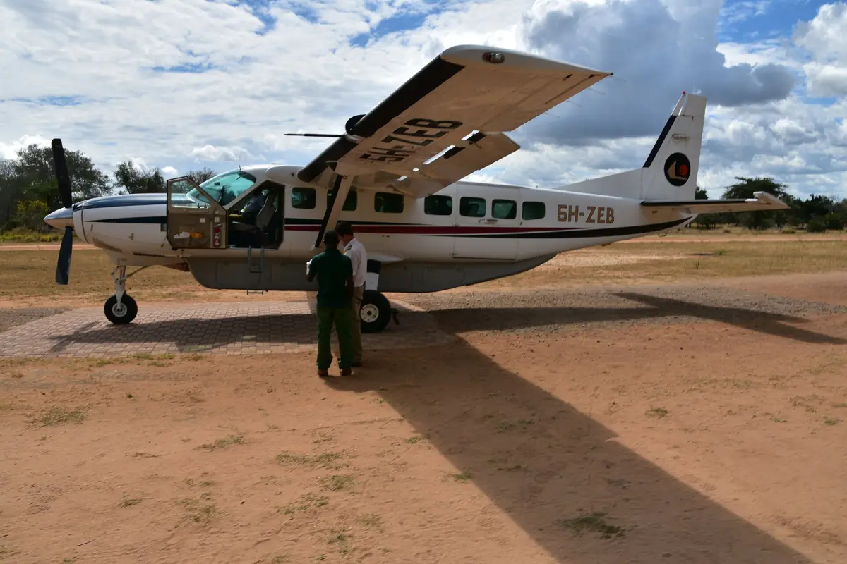 Small propeller plane parked on a bare bush airstrip under clouds