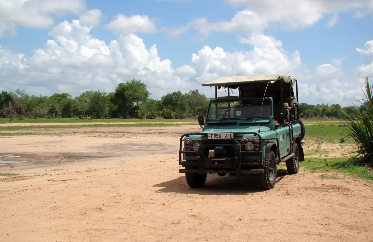 Open safarivoertuig geparkeerd op een zandige open plek met struikgewas